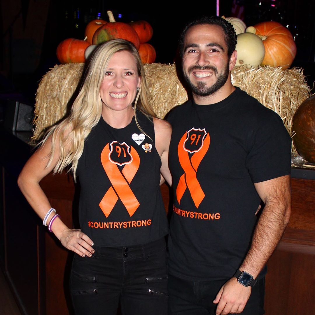 A couple wearing black and orange shirts in front of a stage. 