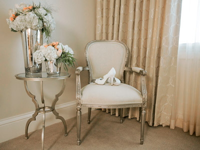 A lounge chair with a pair of the bride's heels on them, next to a a glass table with floral arrangements.