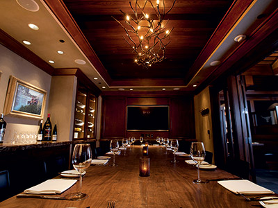 The Carolina Room, featuring with a long dining table, chandelier, built-in wine cabinets, counter, and tv monitor.