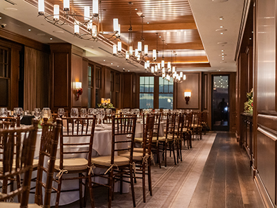 A long formal dining arrangement with multiple round tables, wood flooring, white tablecloths, and evenly spaced chandeliers creating a refined atmosphere.