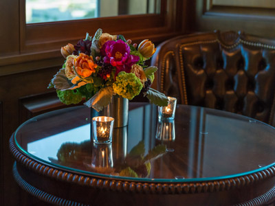 A wooden round table set with flowers and candles, next to a leather chair.