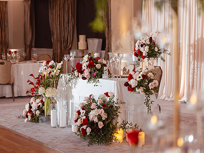 A close view of a sweetheart table adorned with lush floral arrangements, candles, and soft draping set within a warmly lit reception hall.