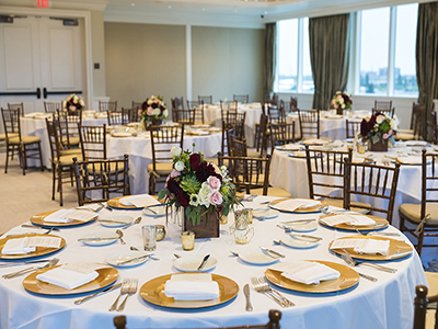 A close view of a round table place setting with white linens, gold charger plates, folded napkins, candles, and floral centerpiece.