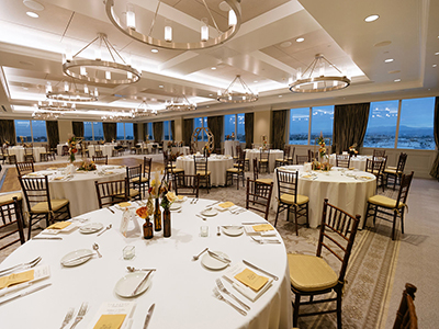 A refined ballroom set with round banquet tables, white linens, lush floral centerpieces, cushioned chairs, and sleek modern chandeliers.