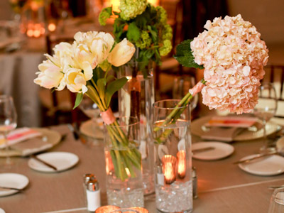 A round table set with glassware, flatware, pink and white flowers, and candles.