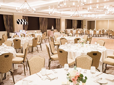 A banquet room arranged for a reception with round tables, white tablecloths, neutral-toned chairs, and soft lighting throughout the space.