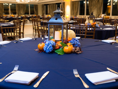 A closeup of a round table and a centerpiece consisting of a lantern and tiny pumpkins and lilacs.