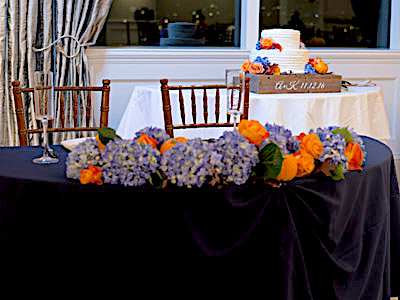 A closeup of the bride and groom's table, decorated with lilacs, orange roses, and tiny pumpkins.