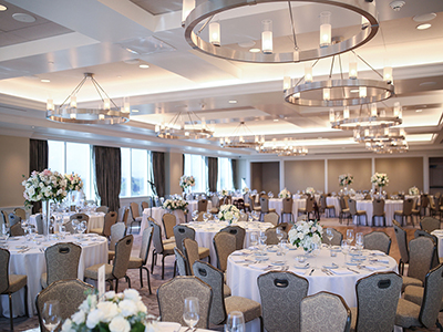 A formal wedding reception layout with an open wood dance floor, round tables along the perimeter, white linens, and warm ambient lighting.