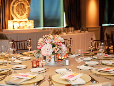 A round table set with glassware, flatware, pink and white flowers, candles, and a buffet table behind it.