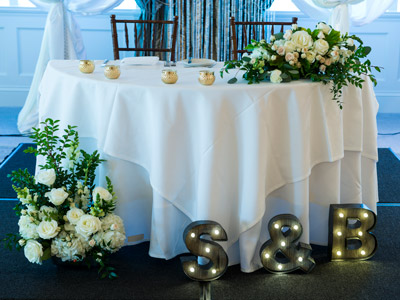 The bride and groom's table, decorated with flowers, candles, and lights of the couples' initials.