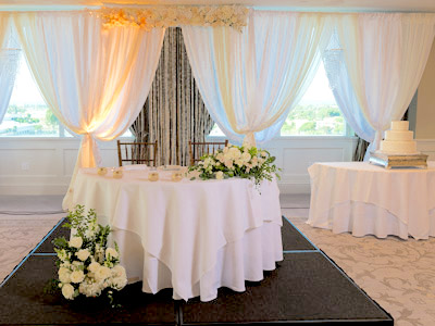 A front view of the bride and groom's table decorated with white roses and the wedding cake table.