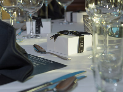 A closeup of a table setting with glassware, flatware, black menu, napkin, and gift boxes.
