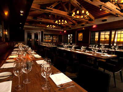 A wood-paneled room with long dining tables, chairs, a bar, and windows.