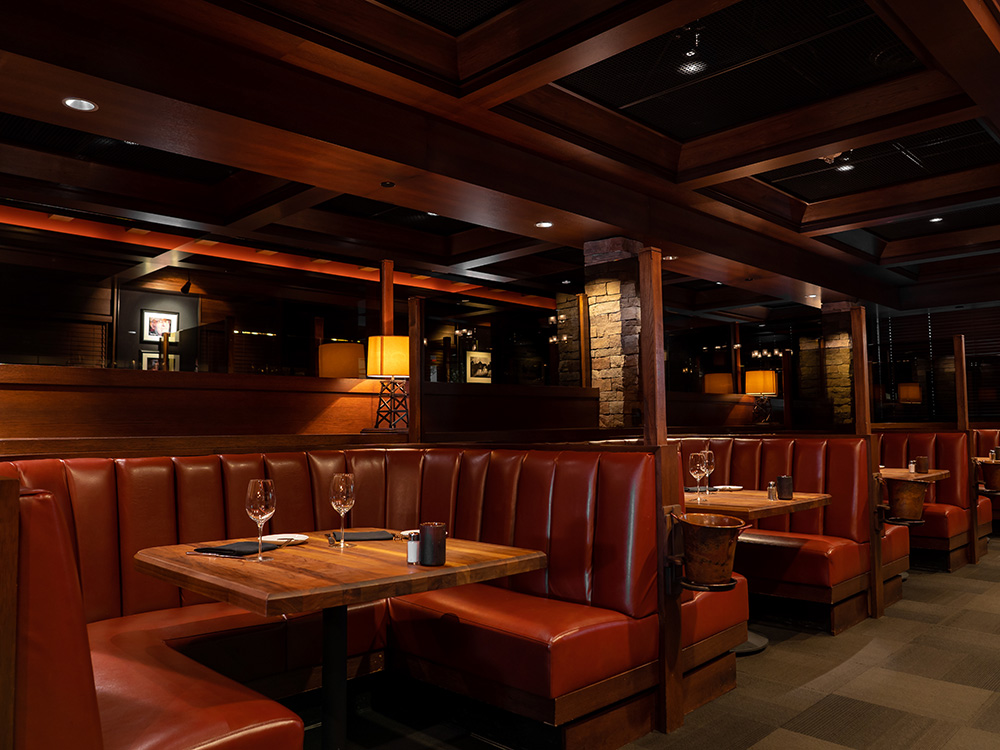 Restaurant dining area with leather booths, polished wood tables, and soft overhead lighting.