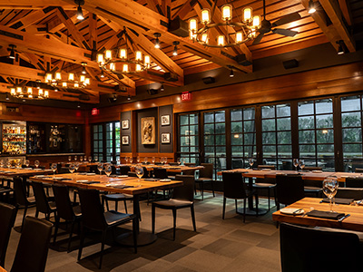 Large dining room with exposed wood beams, chandeliers, and long tables set for dinner service.