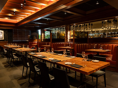 Upscale restaurant interior featuring long communal tables, leather banquettes, and exposed wood ceiling.