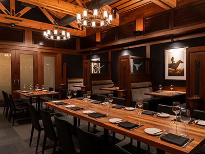 Refined dining room with a long wooden table, chandeliers, and enclosed seating areas.