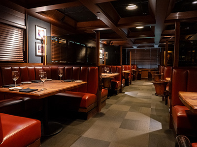 Cozy restaurant booths with polished wood tables and glassware in soft evening lighting.