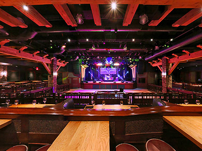 Inside the Ranch Saloon showing a wooden dance floor, stage, guitar disco ball, wooden tables and chairs, and booth seating.