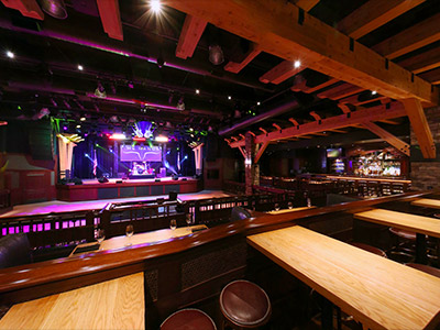 Inside the Ranch Saloon showing a wooden dance floor, stage, guitar disco ball, tables and chairs, and a bar.