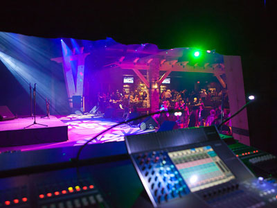 A sound booth looking at a stage with a crowded dance floor below