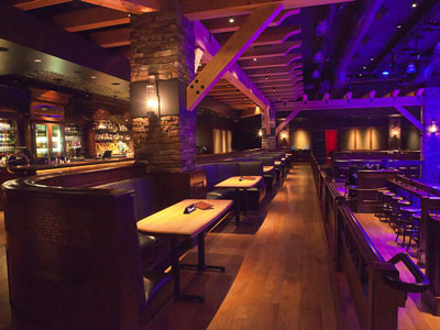 A row of booth seating located between a bar and a dance floor surrounded by wooden stools.