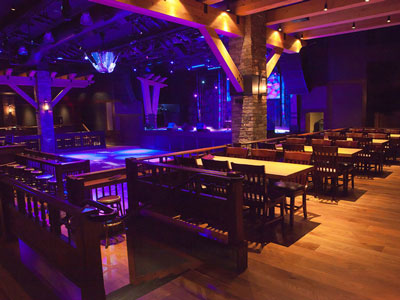 A row of wooden tables and chairs overlooking a dance floor, stage, stools, and guitar disco ball.