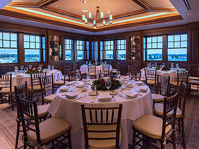 A refined event space with round dining tables, wooden chairs, large windows, and soft ambient lighting highlighting the wood-paneled interior.