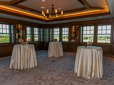 A cocktail-style reception space with tall round tables draped in white linens, small floral arrangements, and expansive windows overlooking the surrounding area.